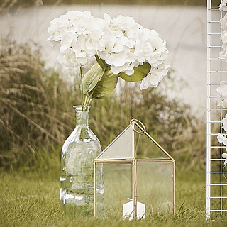 witte hortensia in een transparant glazen vaasje staat in een grasveld naar een gouden windvanger