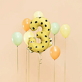 folieballon cijfer 3 geel met zwarte stippen voor een pasteloranje achtergrond met oranje, groene en gele helium ballonnen