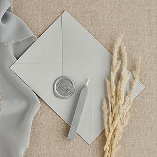 witte envelop met zilveren wax stempel ligt op een jute kleed naast graan en een zilveren laken