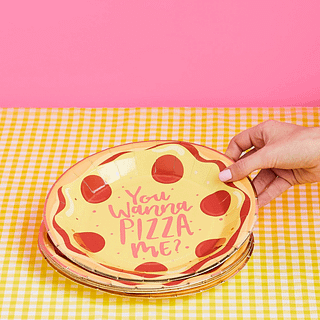 Bordje met pizza bedrukking en de tekst you wanna pizza me op een geel tafelkleed bij een roze muur