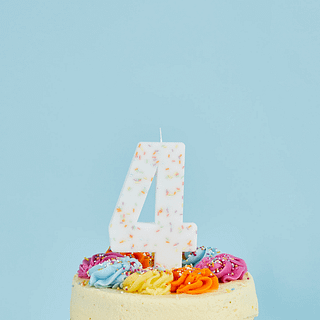 Kaars cijfer 4 met regenboog pastel sprinkles in een witte taart voor een lichtblauwe achtergrond
