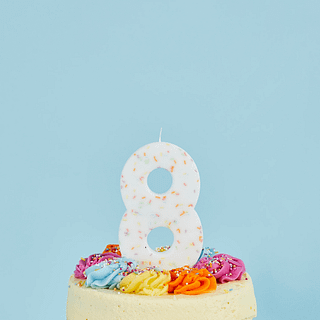 cijfer 8 wit met regenboog sprinkles zit in een taart voor een pastelblauwe muur