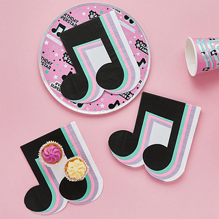papieren servet in de vom van een zwarte muzieknoot met mintgroene, paarse en pastelroze strepen liggen op een roze achtergrond en zijn bedekt met cupcakes