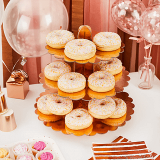 rose gouden standaard met drie verdiepingen is gevuld met donuts en omrings door rose gouden versiering