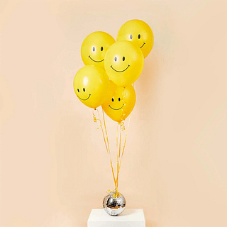 Gele smileyballonnen zweven voor een perzikkleurige muur en hangen aan een zilveren discobal