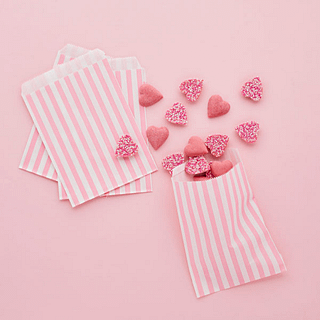 roze achtergrond met roze en wit gestreepte zakjes gevuld met snoep hartjes