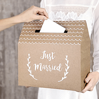 bruine kaartendoos in de vorm van een huisje met witte versiering en de tekst just married word vastgehouden door een vrouw in trouwjurk