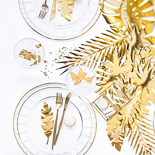 gouden bladeren liggen op een wit versierde tafel met witte borden met een gouden rand en gouden bestek