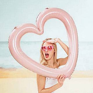 vrouw met roze zonnebril staat op het strand met een roze hartvormige ballon