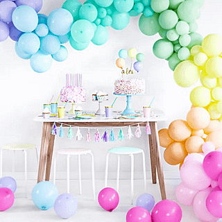 Pastel ballonnenboog met regenboog ballonnen hangt boven een houten tafel voor een witte muur