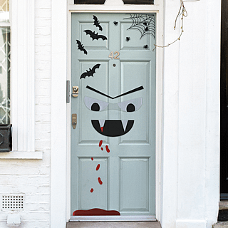 Deurstickers met een vampiergezichtje, spinnen, spinnenwebben, bloeddruppels en vleermuizen zitten op een mintgroene deur in een wit huis