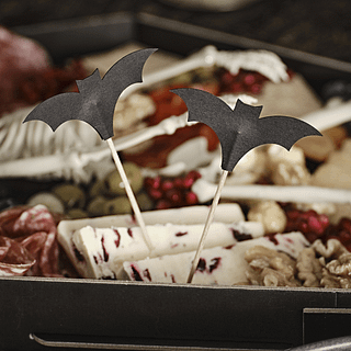 Sateprikkers met een zwarte vleermuizen eraan zitten in een bord gevuld met olijven, droge worst, walnoten en cake