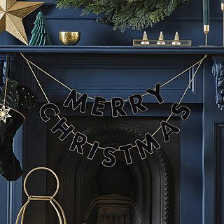 Zwarte velvet slinger met de tekst merry christmas met gouden details hangt voor een donkerblauwe openhaard