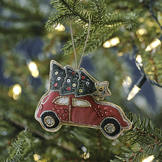 Kerstboomhanger in de vorm van een rode auto met een groen kerstboompje op het dak hangt in de boom