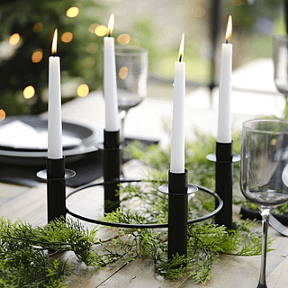 Zwarte kaarsenhouder voor vier kaarsen staat op een groen hulst blad op een houten tafel