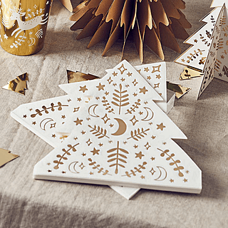 Servetten in de vorm van een kerstboom met goudenprint liggen op een katoenen beige kleed