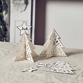 Tafelkaartjes in de vorm van een kerstboom in het wit en goud liggen op een katoenen kleed