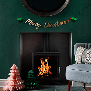 kerstslinger met gouden tekst merry christmas en groene hulst met rode besjes hangt boven een vuur aan een donkergroene muur