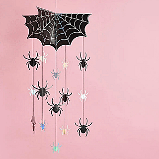 Zwart spinnenweb met zwarte en iridescent spinnen hangt voor een lichtroze achtergrond
