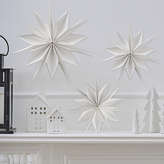 Witte, papieren sterren hangen boven een witte schoorsteen naast stenen huisjes en kerstboompjes