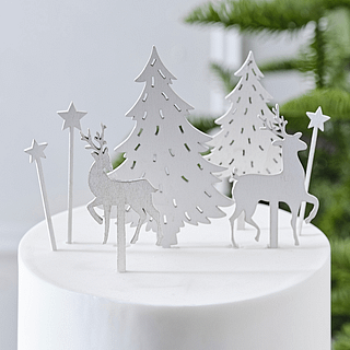 Witte, houten taart toppers in de vorm van dennenbomen, sterren en rendieren staan op een witte, gladde taart