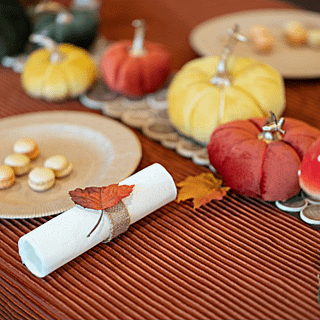 Stoffen herfstbladeren confetti ligt op een bruine tafel versierd met stoffen pompoenen