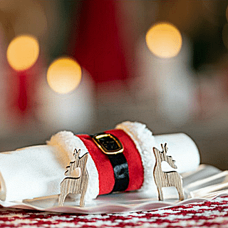 Servet ligt in een servettenring die lijkt op het pak van de kerstman achter twee houten hertjes