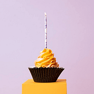 Taart kaarsje met marmer effect in het paars en wit zit in een gele cupcake voor een paarse muur