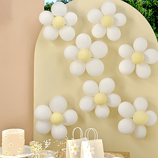 Madelief ballonnen in het wit en pastel geel zitten aan een kartonnen boog en staan achter een bijpassende taart en madelief cadeau tasjes