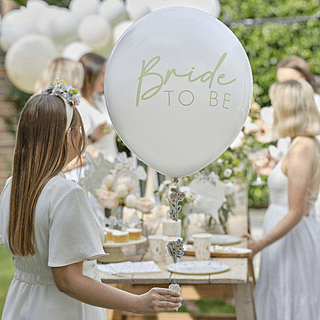 Grote ballon in het saliegroen met de tekst bride to be en bloemen word vastgehouden door een dame met bruin haar in een witte jurk en een bloemen haarband