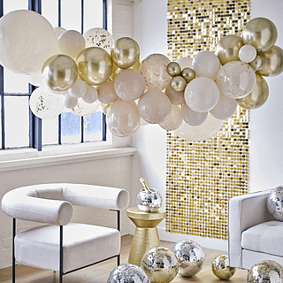 Ballonnenboog met nude, gouden en witte ballonnen hangt voor een gouden backdrop en disco ballen in het goud en zilver
