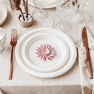 Tafel versierd met goud bestek, witte borden en roze bloemen