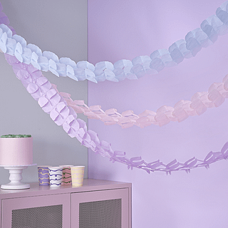 Crep[e papier slingers in het lila, lichtroze en pastel blauw hangen voor een lila muur en roze kastje
