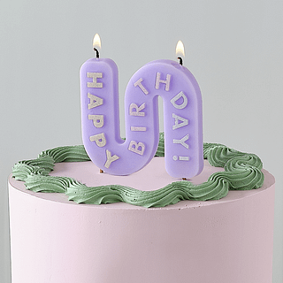 Lila kaars met de tekst happy birthday erop zit in een roze taart met groene rand
