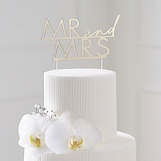 Gouden cake topper van acryl met de tekst mr and mrs zit in een witte taart met bloemen