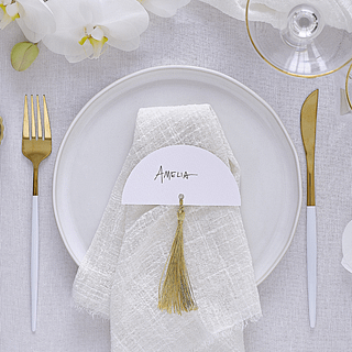 Wit tafelkaartje met een gouden tassel ligt op een witte, stoffen servet