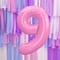 Folieballon cijfer 9 in het roze voor een muur bedekt met franjes in de kleuren paars, lichtblauw, wit en roze