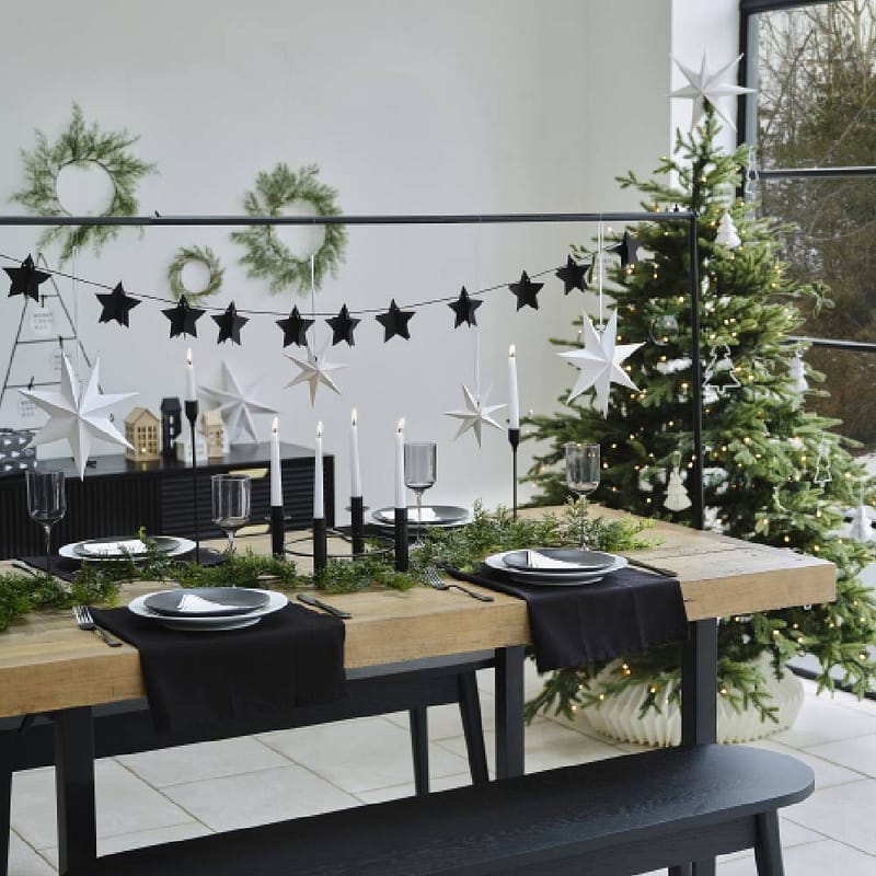 Gedekte tafel met tafelstandaard erboven met sterrenslinger en andere kerstversiering en een kerstboom