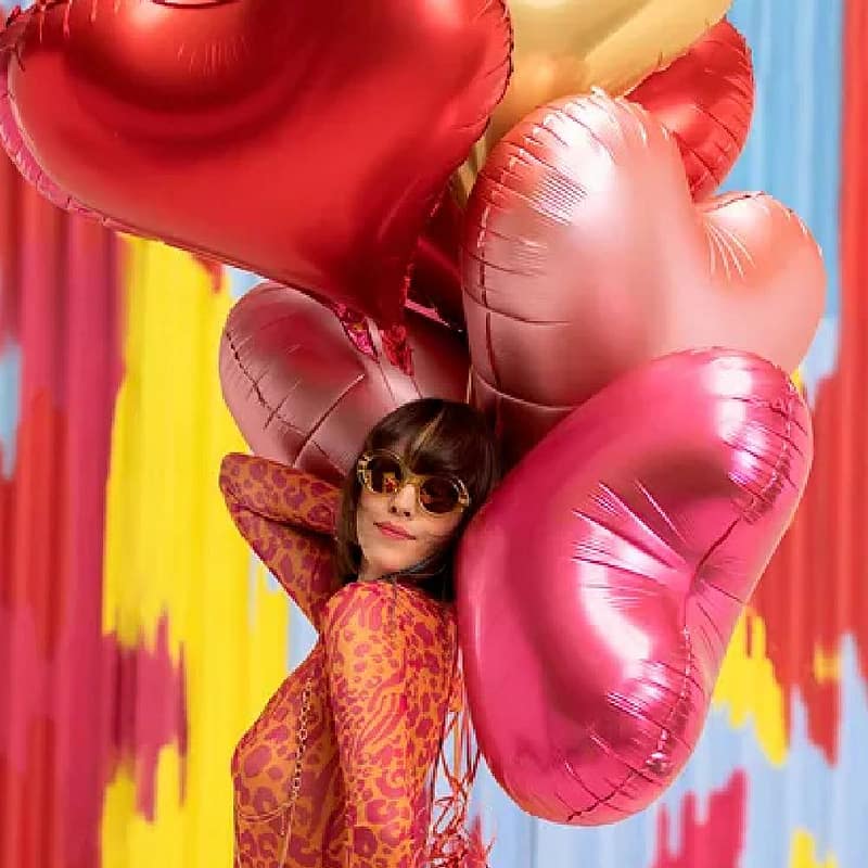 Vrouw met een tros hartvormige ballonnen in de kleuren rood, roze, rosé goud en goud
