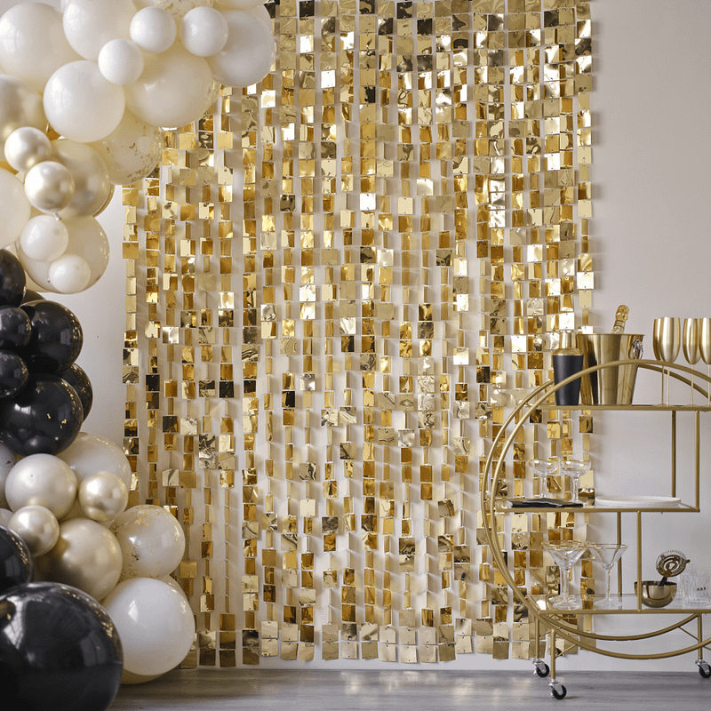 Metalen backdrop met gouden vierkantjes hangt voor een nudekleurige muur en achter een ballonnenboog met nude, zwarte en champagnegouden ballonnen