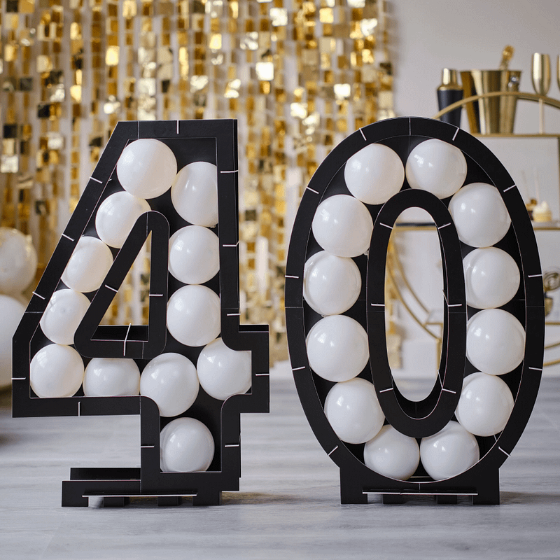 Ballonstandaard in de cijfers 40 in het zwart gevuld met witte ballonnen staat voor een gouden backdrop