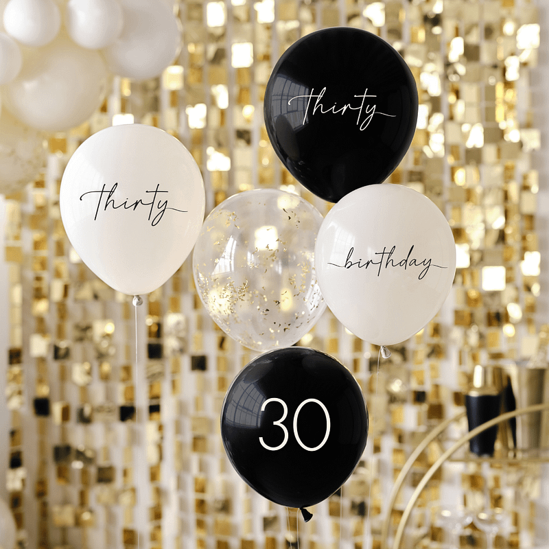 Ballonnen voor 30 jaar in het zwart en nudekleurig met een transparante confettiballon met gouden confettisnippers zweven voor een gouden backdrop met vierkantjes