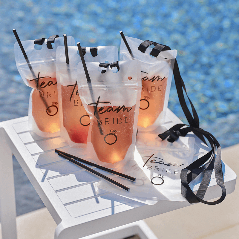 Transparante afsluitbare drinkzakjes met zwarte rietjes staan op een wit tafeltje naast een zwembad