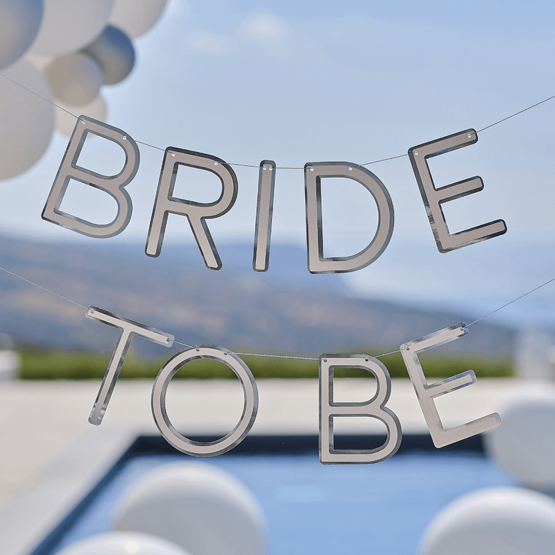 Zilveren slinger met de tekst bride to be hangt voor een zwembad met witte ballonnen
