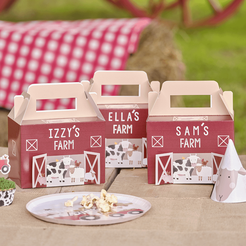 Partyboxen in de vorm van boerderijen staan op een houten tafel achter een bordje met popcorn en een feesthoedje in de vorm van een schaapje