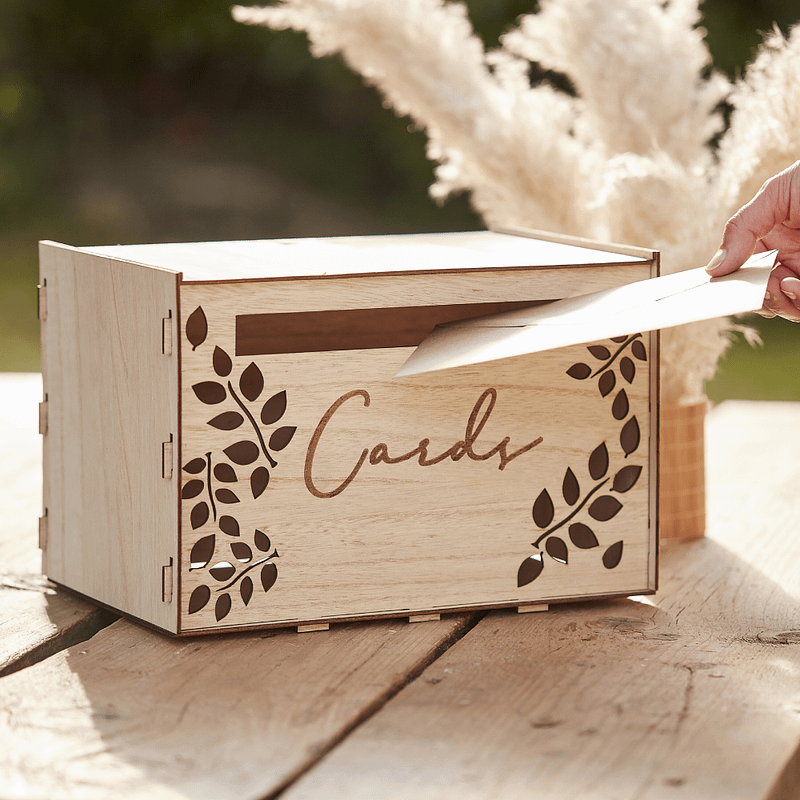 houten doos met de tekst cards en bladeren erop voor enveloppen staat op een picknicktafel naast wat pampas
