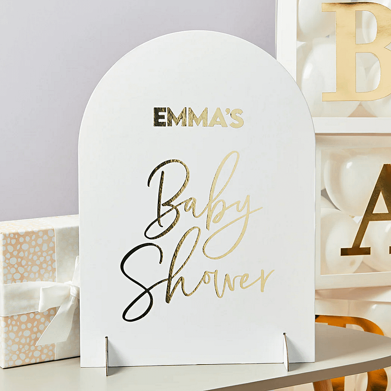 wit bord met gouden tekst emma's babyshower staat voor gouden en witte blokken op een houten tafel