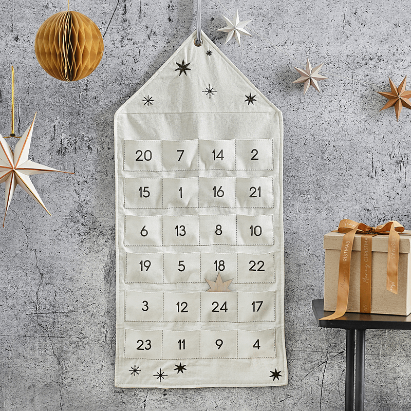Katoenen advent kalender in de vorm van een huisje met 24 zakjes en zwarte sterren hangt voor een grijze muur naast een koperen honeycomb en ster