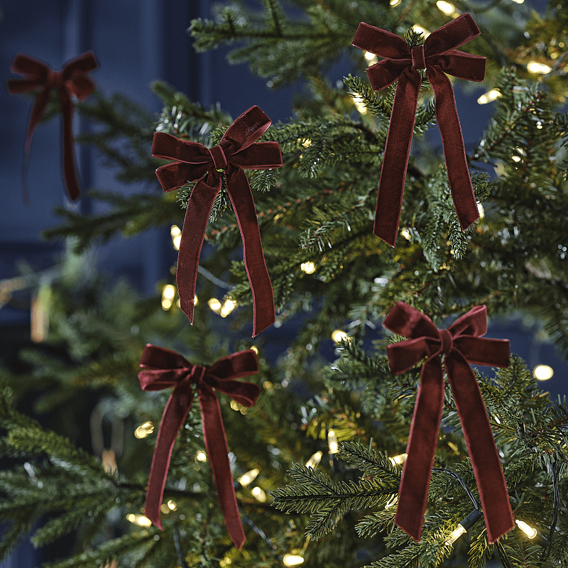 Donkerrode velvet strik hangt in een kerstboom met lampjes voor een donkerblauwe muur
