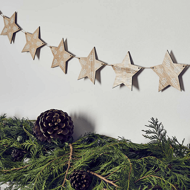 Slinger met houten sterren hangt boven groene versiering en een dennenappel